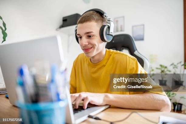 jovem sorridente sentado em uma mesa e jogando um jogo em um laptop - apple tv - fotografias e filmes do acervo