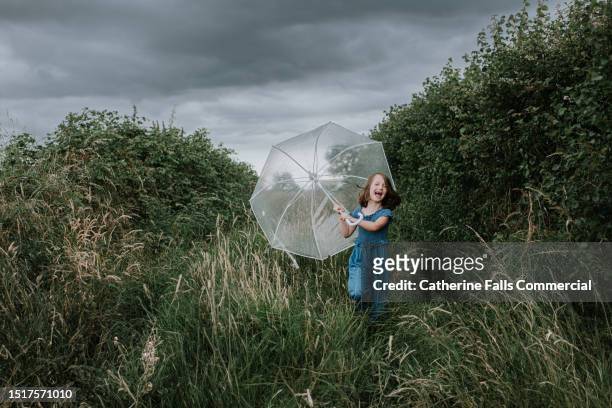 a little girl squeals happily and runs towards the viewer, clutching an umbrella, as rainfall begins - see through shoe stock pictures, royalty-free photos & images