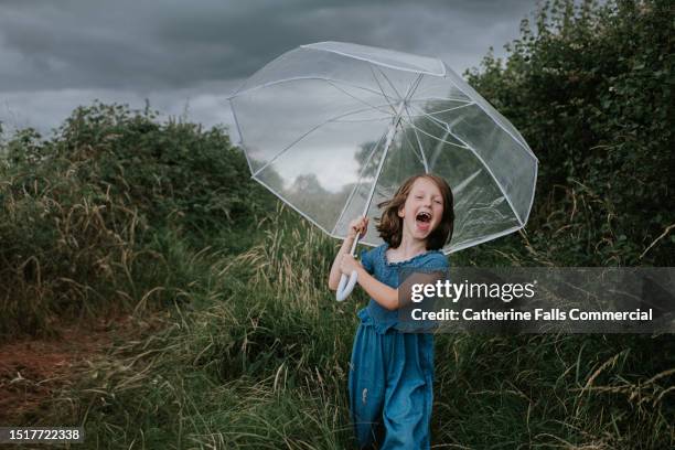 a little girl looks joyful, under an umbrella, despite an approaching rain storm - see through shoe stock pictures, royalty-free photos & images