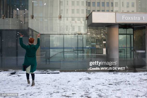 Woman throws snow in the air at a plaza in front of an office building in Johannesburg on July 10, 2023.