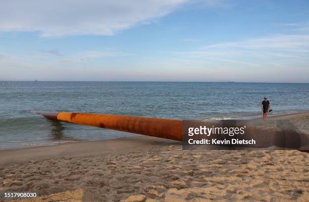 Man walks near a pipe from a sand pumping barge off-shore as the Army Corps of Engineers continues their beach and dune replenishment project on July...
