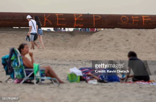 Beachgoers walks past a section of pipe from a sand pumping barge off-shore as the Army Corps of Engineers continues their beach and dune...