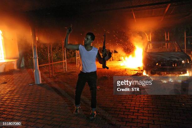 An armed man waves his rifle as buildings and cars are engulfed in flames after being set on fire inside the US consulate compound in Benghazi late...