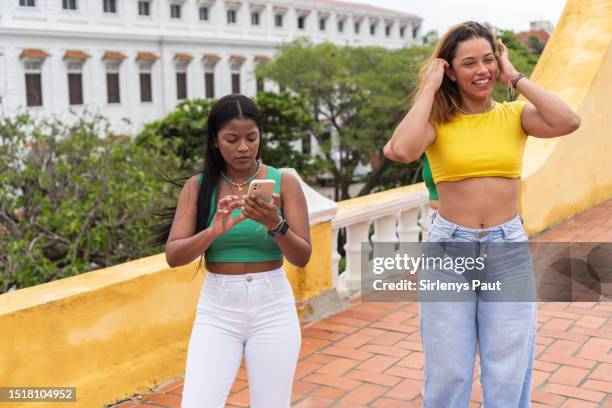 beautiful latina women having fun on the street. woman checks smart phone - amigos baile stockfoto's en -beelden