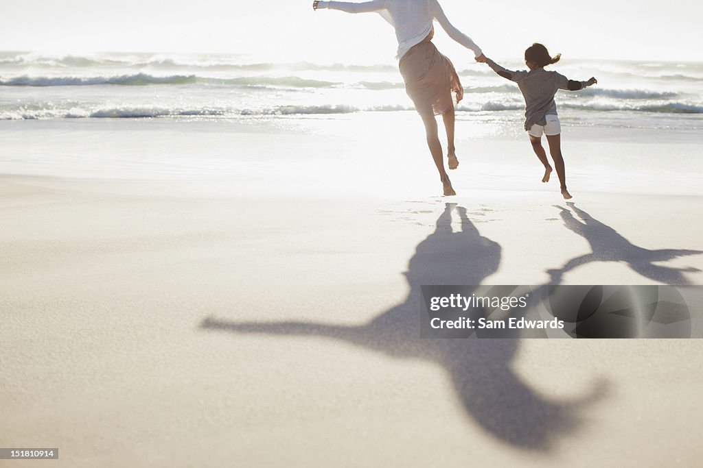 Mother and daughter holding hands and running on sunny beach