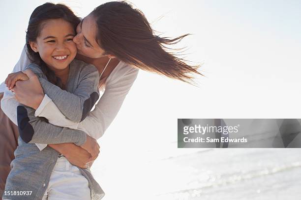 mother hugging and kissing daughter on beach - asian mom kid kiss stock-fotos und bilder