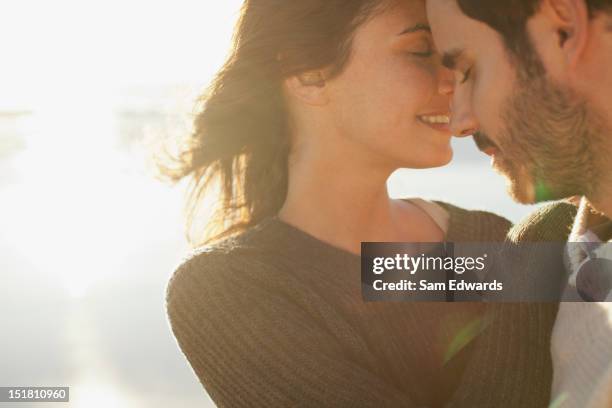 sun shining behind couple hugging with eyes closed - sun flare couple stock-fotos und bilder