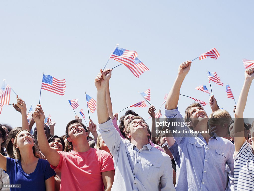 Smiling people waving American flags and looking up in crowd