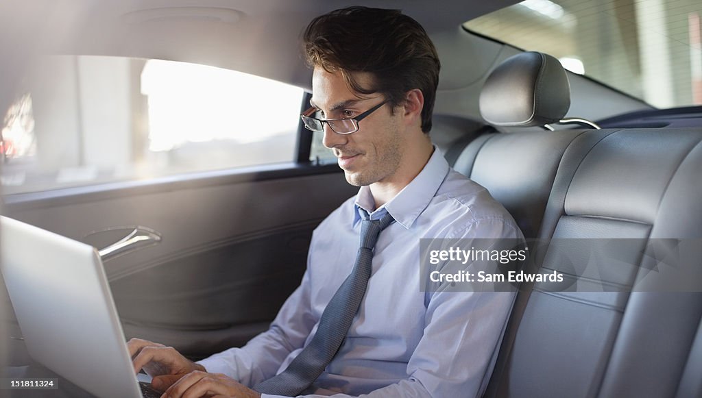 Uomo d'affari utilizzando il computer portatile nel sedile posteriore dell'auto