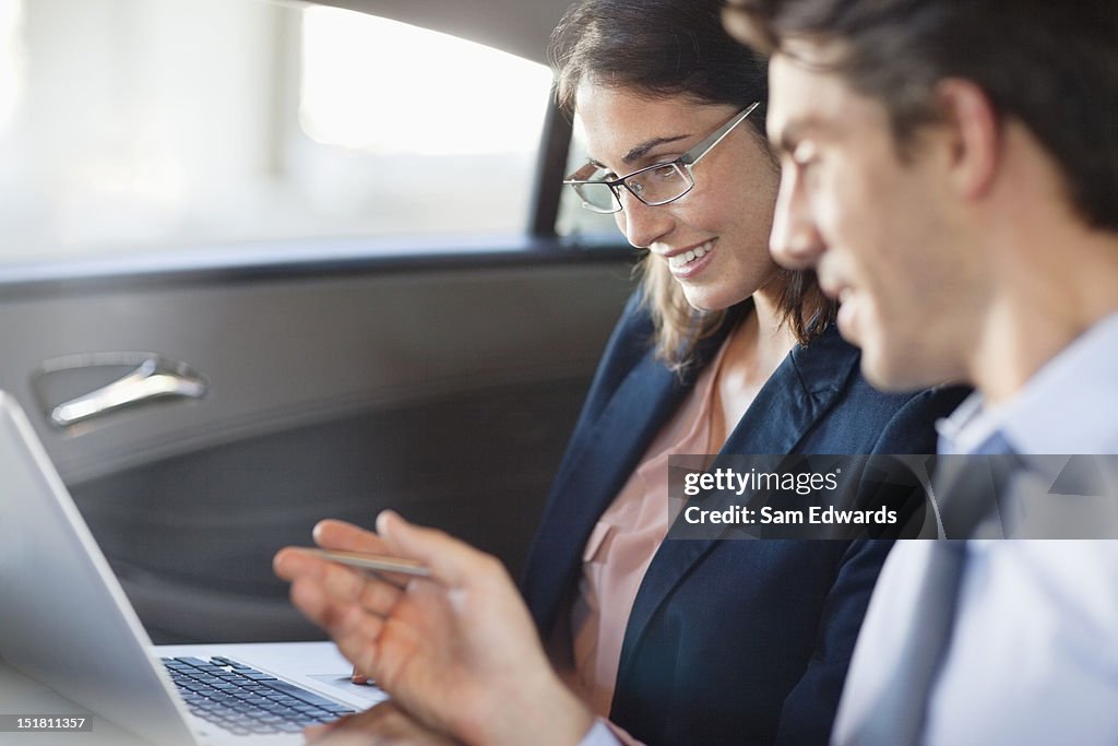 Businessman and businesswoman using laptop in back seat of car