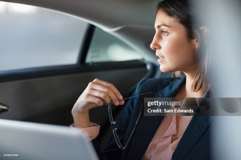 Pensive businesswoman with laptop in back seat of car