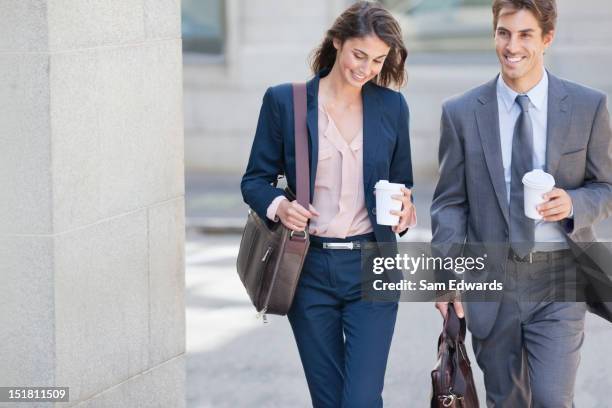 smiling businessman and businesswoman walking with coffee cups - young adults coffee stockfoto's en -beelden