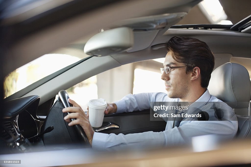 Businessman holding coffee cup and driving car