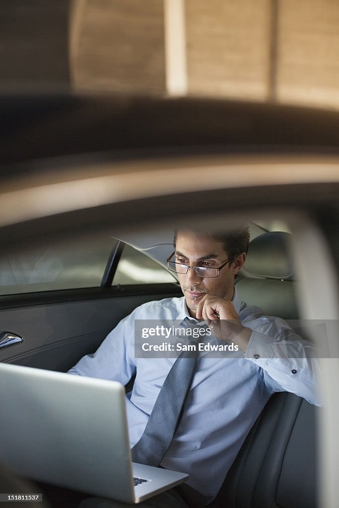 Businessman working on laptop in back seat of car at night