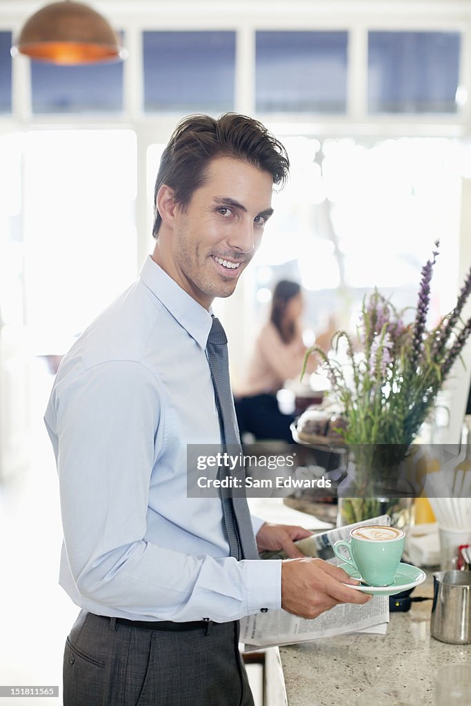 Portrait of smiling businessman with coffee and newspaper in cafe