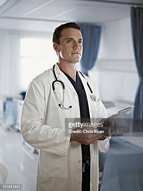 portrait of confident doctor holding medical record in hospital room - three quarter length stockfoto's en -beelden