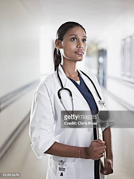 portrait of pensive doctor holding medical record in hospital corridor - three quarter length stock pictures, royalty-free photos & images