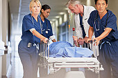 Doctor and nurses wheeling patient in gurney down hospital corridor