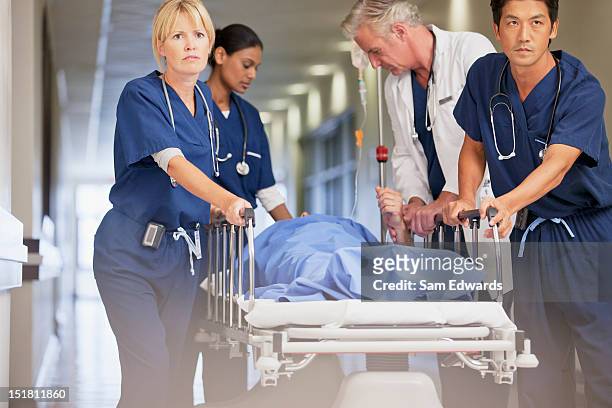 doctor and nurses wheeling patient in gurney down hospital corridor - accidents and disasters stock pictures, royalty-free photos & images