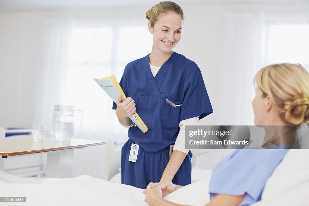 Krankenschwester mit medizinischen Aufzeichnungen im Gespräch mit Patienten im Krankenhaus Zimmer