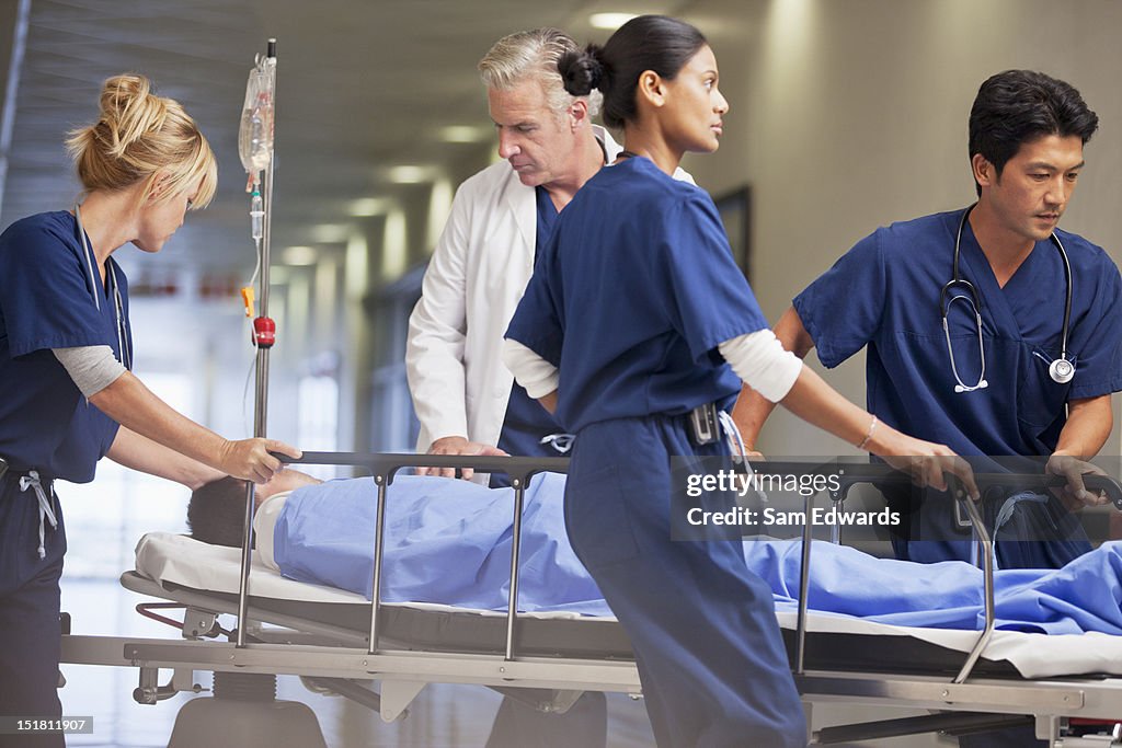 Doctor and nurses wheeling patient in gurney through hospital corridor