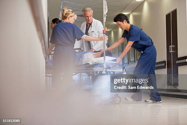 doctors and nurses wheeling patient on gurney in hospital corridor - pushing stretcher stock pictures, royalty-free photos & images