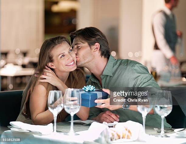 man kissing and giving gift to woman in restaurant - anniversary stock pictures, royalty-free photos & images