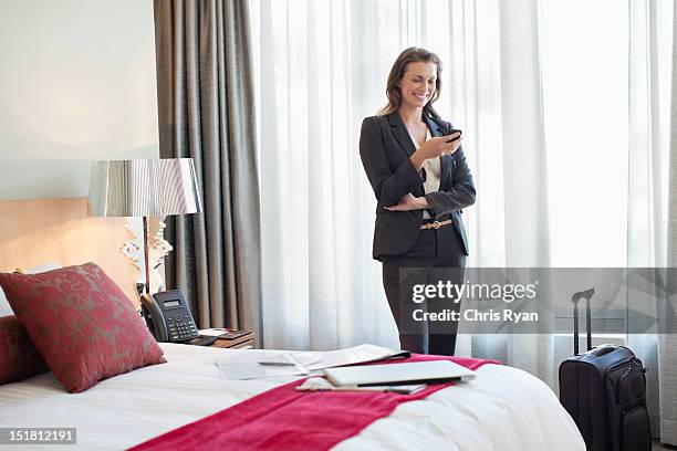 smiling businesswoman checking cell phone in hotel room - businesswoman hotel stock pictures, royalty-free photos & images