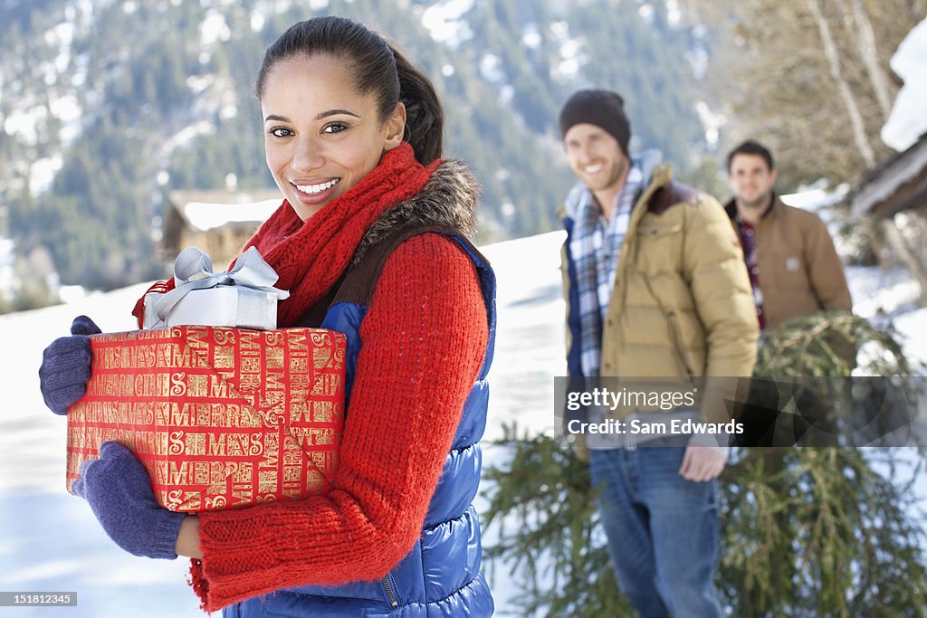 Portrait of friends with fresh cut Christmas tree and gifts in snow