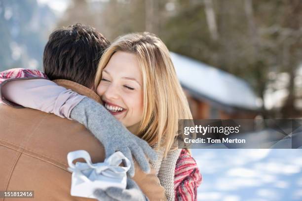 smiling woman holding christmas gift and hugging man in snowy field - hug christmas stock pictures, royalty-free photos & images