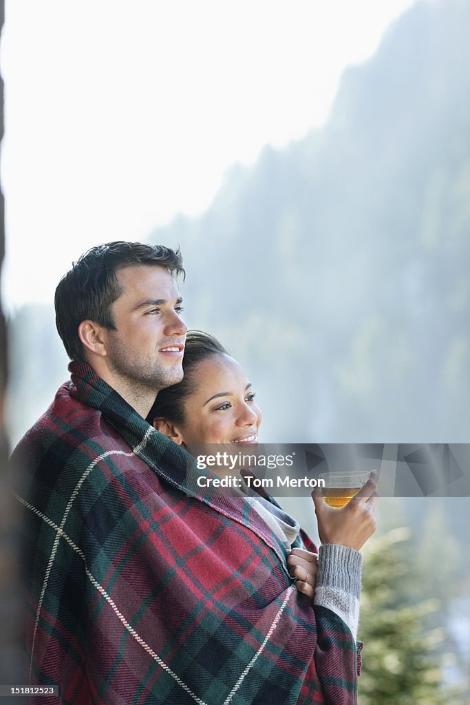 Sonriente pareja envuelto en una manta y bebiendo té al aire libre