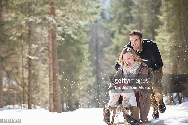 man pushing woman on sled in snowy woods - girlfriend getaway stock pictures, royalty-free photos & images
