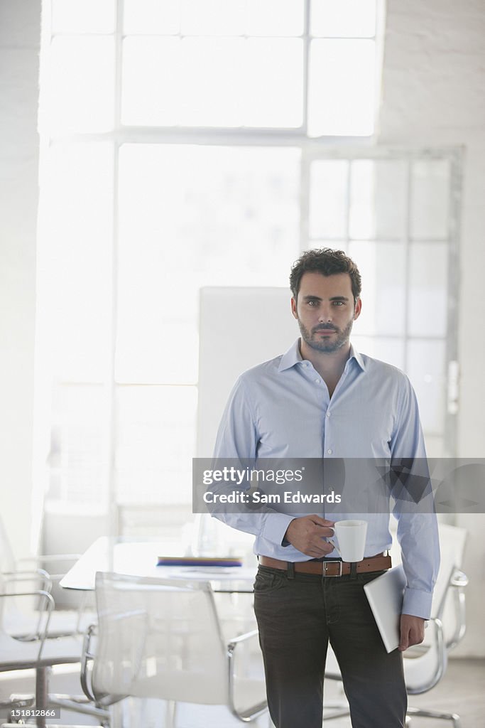 Portrait of serious businessman holding coffee cup and digital tablet in office