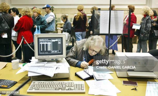 Senior citizen fills out a form in order to recieve her retirement pension, while other retired and unemployed citizens wait in line at a branch of...