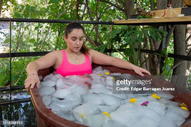 young mexican woman inside a tub doing an ice bath on the terrace of a yoga studio - ice bath stock pictures, royalty-free photos & images