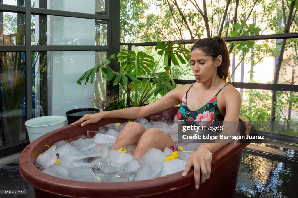 A young Mexican woman doing an ice bath or cryotherapy on the terrace of her apartment inside a tub