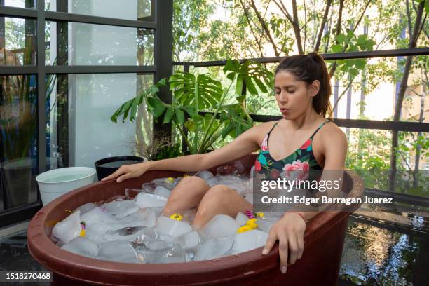 a young mexican woman doing an ice bath or cryotherapy on the terrace of her apartment inside a tub - ice bath stock pictures, royalty-free photos & images