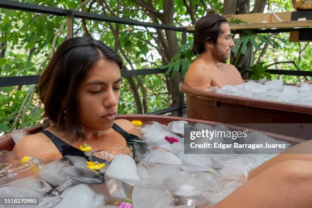 a man and a woman are taking an ice bath in a tub on the outdoor terrace - ice bath stock pictures, royalty-free photos & images