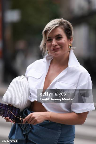 Anna Stukkert is seen wearing big sunglasses with a golden frame, golden earrings with a blue/white eye on it, a white short-sleeved cropped shirt...