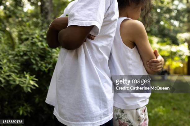 young black boy & young multiracial girl stand back to back with arms crossed - time out stock-fotos und bilder