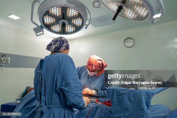 female surgeon and her instrumentalist suture a woman after performing a caesarean section - caesarean section stock-fotos und bilder