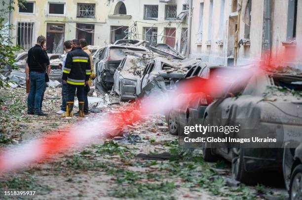 Civilians and a rescuer stand next to damaged vehicles and a four-storey residential building that was struck by a missile attack on July 6, 2023 in...