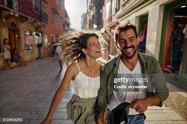 pareja juguetona divirtiéndose mientras corre por la calle. - city 2 fotografías e imágenes de stock