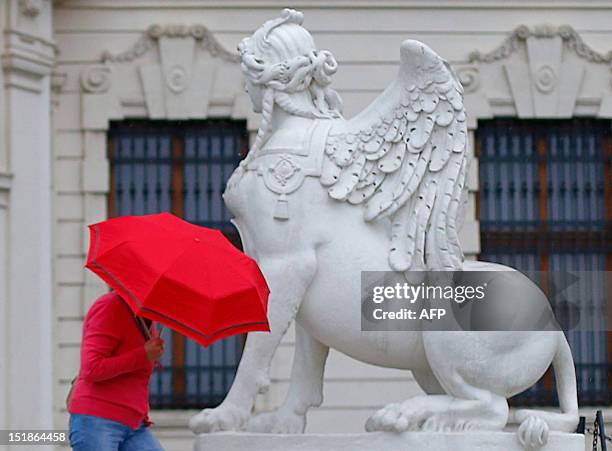 Woman holds a red umbrella as she walks by a statue of a Sphinx at the upper Belvedere Palace on a rainy day in Vienna on September 12, 2012. AFP...