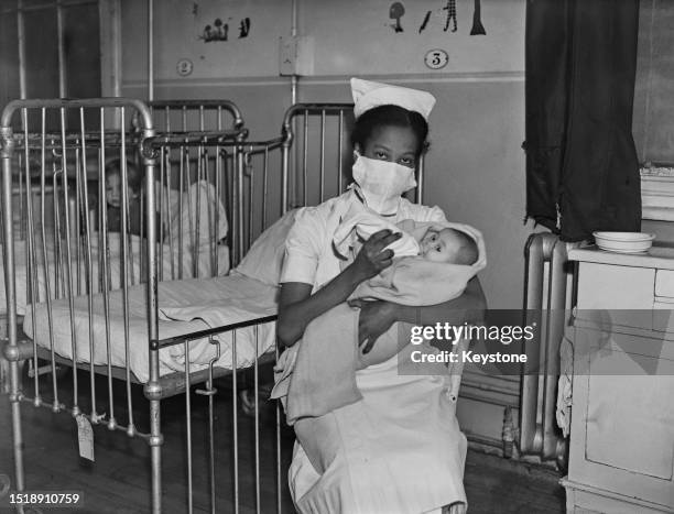Nurse M O'Loughlin from Saint Kitts Island feeding a baby on a hospital children's ward, London, March 14th 1945.