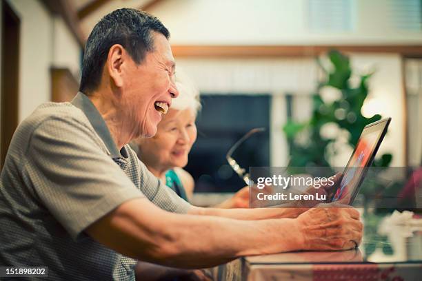senior couple look at photos on tablet happily - chinese couple computer bildbanksfoton och bilder
