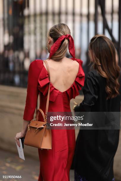 Guest seen outside Zuhair Murad show wearing red hair bow, red open back dress and Hermes Kelly bag in brown with gold hardware during the Haute...