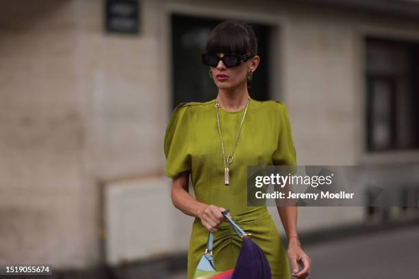 Katya Tolstova is seen wearing black sunglasses from Prada, transparent hoop earrings, a golden necklace, a green midi dress with gathered waist, a...