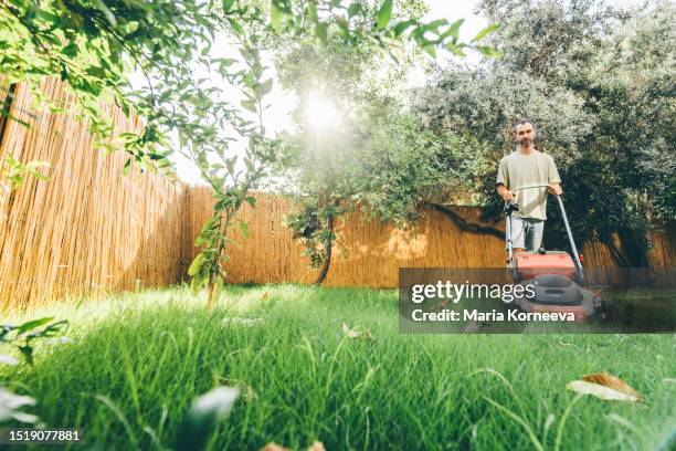 man using a lawn mower in his back yard. - cortar relva imagens e fotografias de stock