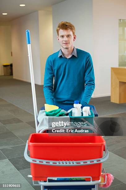 male cleaner pushing trolley with cleaning equipment - reinier stockfoto's en -beelden